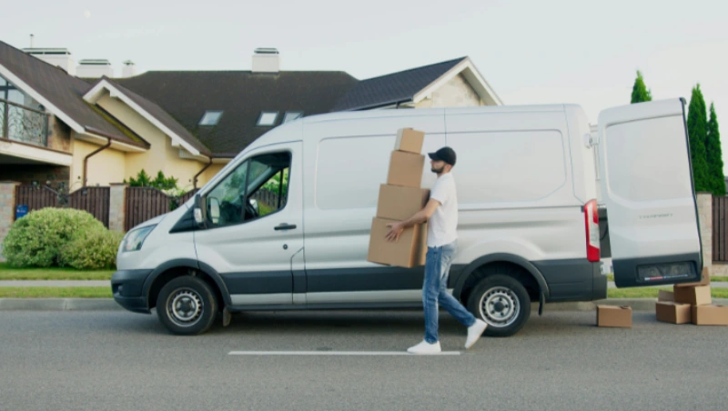 Moving van parked in front of residential villa with movers carrying boxes on sunny day