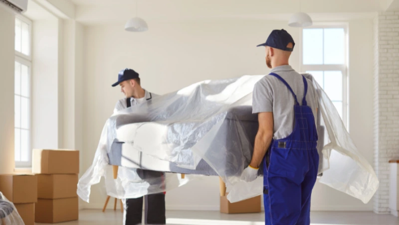 Two movers wrapping furniture with protective plastic covering during villa relocation